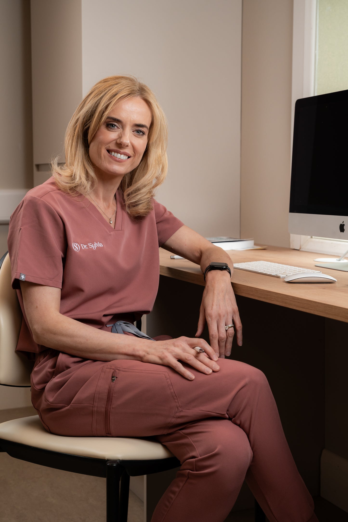 Person in pink scrubs sitting at a desk with a computer in an office setting