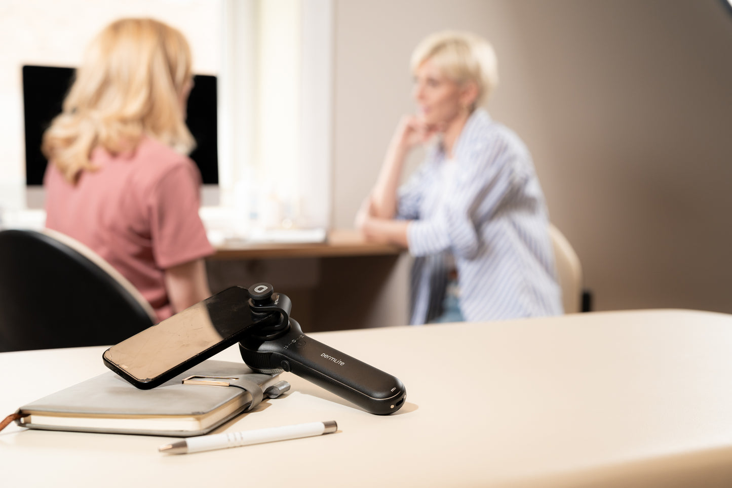Phone with a camera attachment on a desk with two people in the background