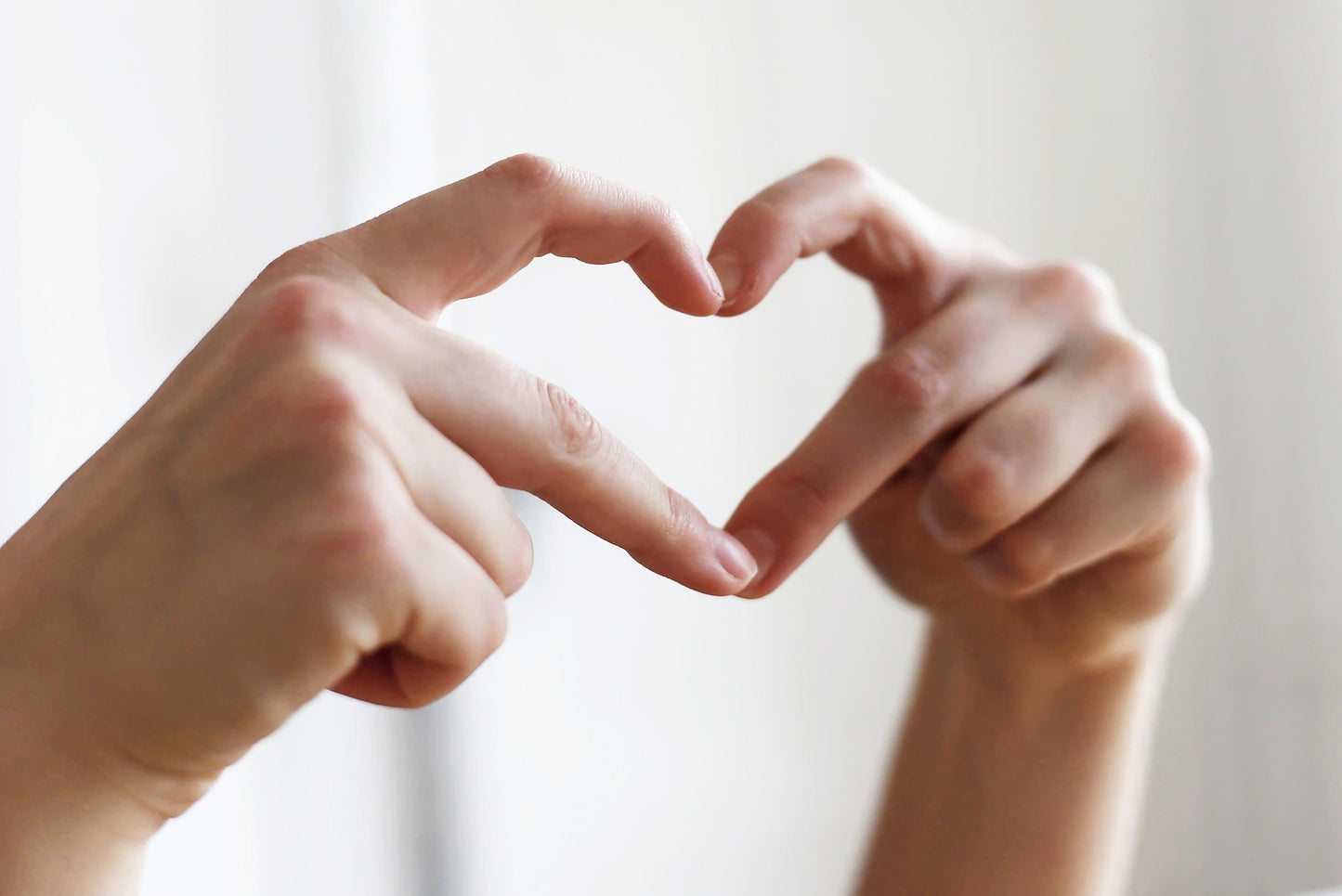 Two hands making a heart shape against a light background
